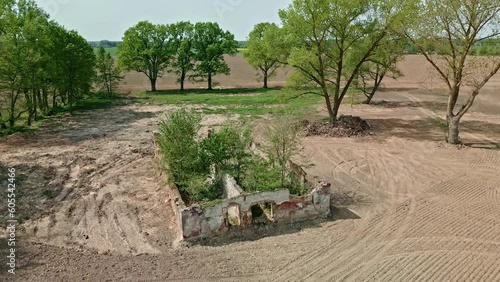 Aerial drone backward moving shot over dilapidated house surrounded by brown ploughed soil preparation for sowing seeds on a sunny day. photo