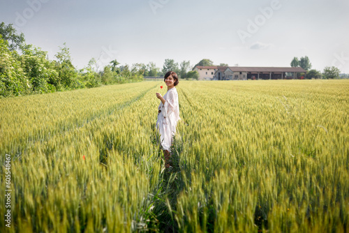 smilig woman with dark hair in white dress walking in grain field