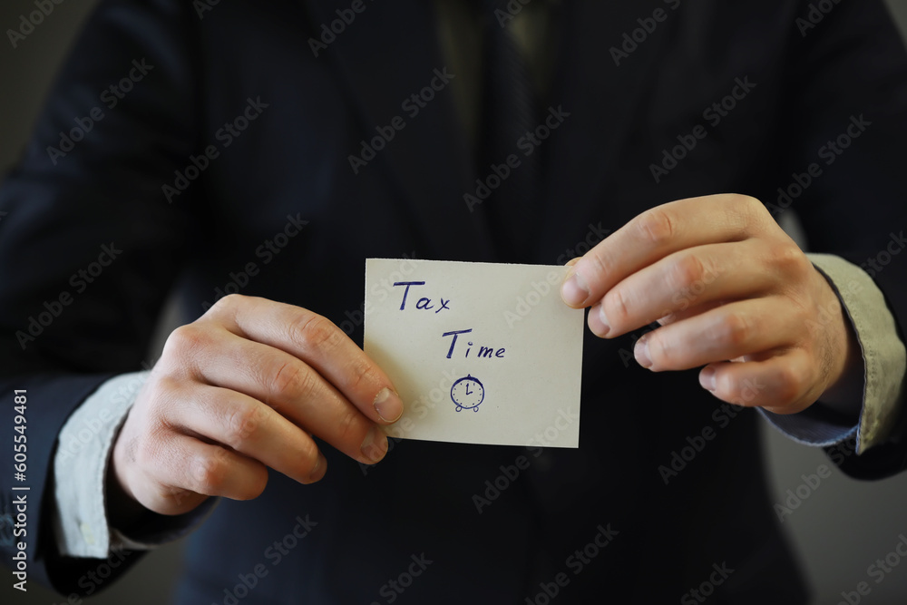 Businessman in a suit hand holding sticker with tax time Businessman in a suit hand holding sticker with tax time