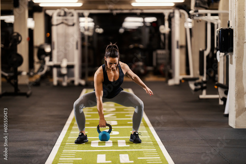Принти на полотні A strong female bodybuilder is squatting in a gym and lifting kettlebell in a gym