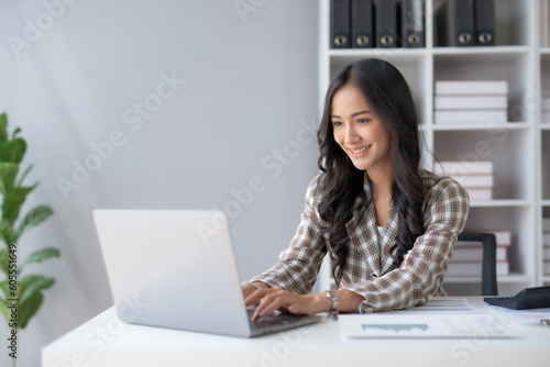 Happy smiling Asian businesswoman using laptop computer in the office. Beautiful young Asian female shopping or chatting online in social networks, freelance working on laptop projects.
