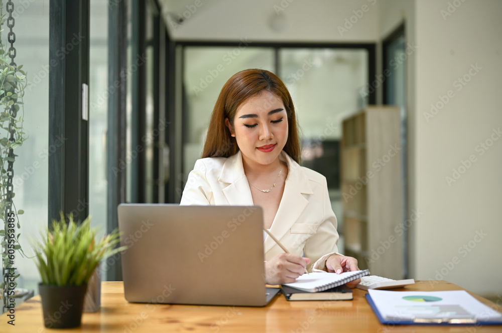 © bongkarn - Beautiful and focused Asian businesswoman writing something on report © bongkarn - Beautiful and focused Asian businesswoman writing something on report