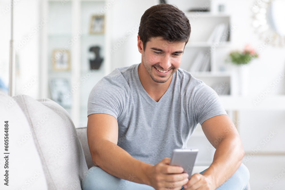 Young handsome happy man use phone on sofa in living room. Write to chat, net surfing.