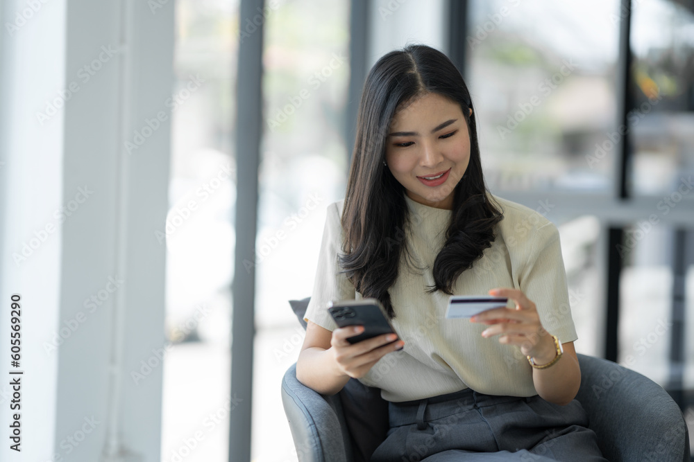 Confident young asian woman using mobile phone to open application using credit card for online shopping while sitting on sofa chair at office. Confident young asian woman using mobile phone to open application using credit card for online shopping while sitting on sofa chair at office.