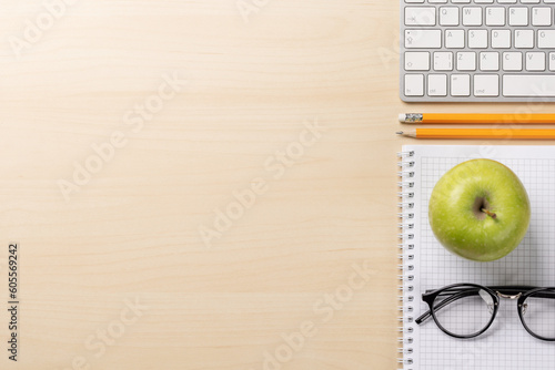 Top view of keyboard, notebook, glasses, pencils, apple