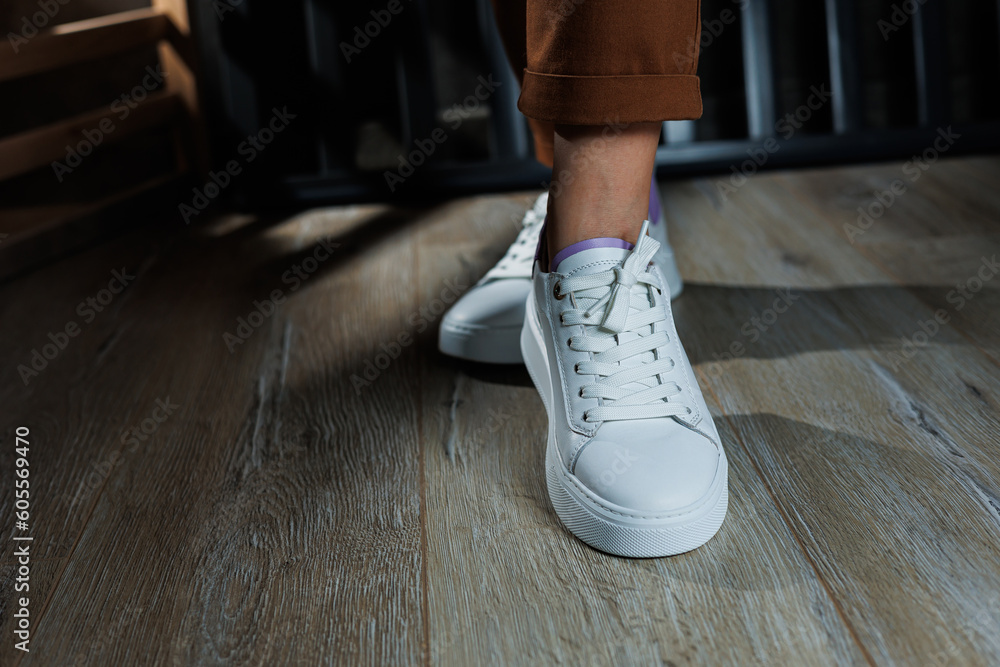Female legs in white leather sneakers with perforations. Collection of summer women's shoes. White women's sneakers with laces Female legs in white leather sneakers with perforations. Collection of summer women's shoes. White women's sneakers with laces