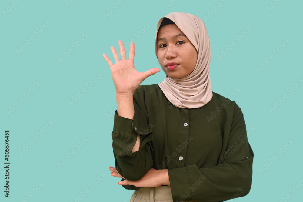 A calm Asian teenager wearing a dark green t-shirt giving number 12345 by hand gesture on blue background. A calm Asian teenager wearing a dark green t-shirt giving number 12345 by hand gesture on blue background.