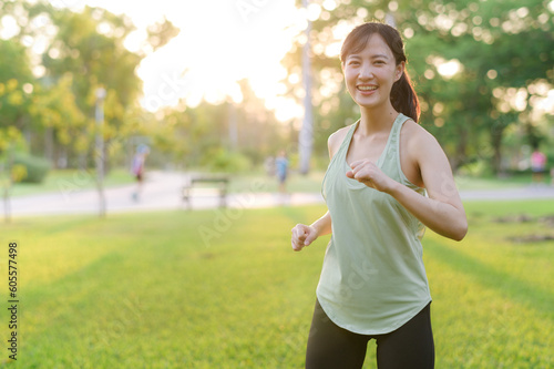 Female jogger. Fit young Asian woman with green sportswear stretching muscle in park before running and enjoying a healthy outdoor. Fitness runner girl in public park. Wellness being concept © Jirawatfoto