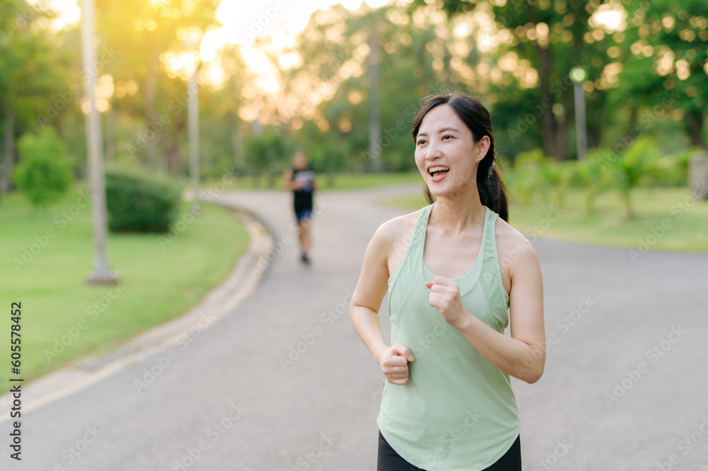 Fit Asian young woman jogging in park smiling happy running and enjoying a healthy outdoor lifestyle. Female jogger. Fitness runner girl in public park. healthy lifestyle and wellness being concept Fit Asian young woman jogging in park smiling happy running and enjoying a healthy outdoor lifestyle. Female jogger. Fitness runner girl in public park. healthy lifestyle and wellness being concept