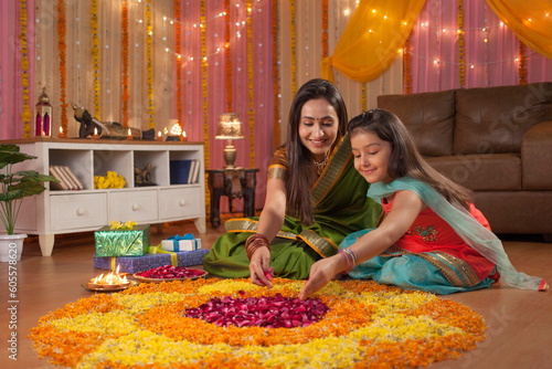 Beautiful mother and daughter making rangoli on diwali festival - Colorful background. Image of mother and daughter putting rose petals in rangoli on occasion of diwali. Posing for the camera with ... photo