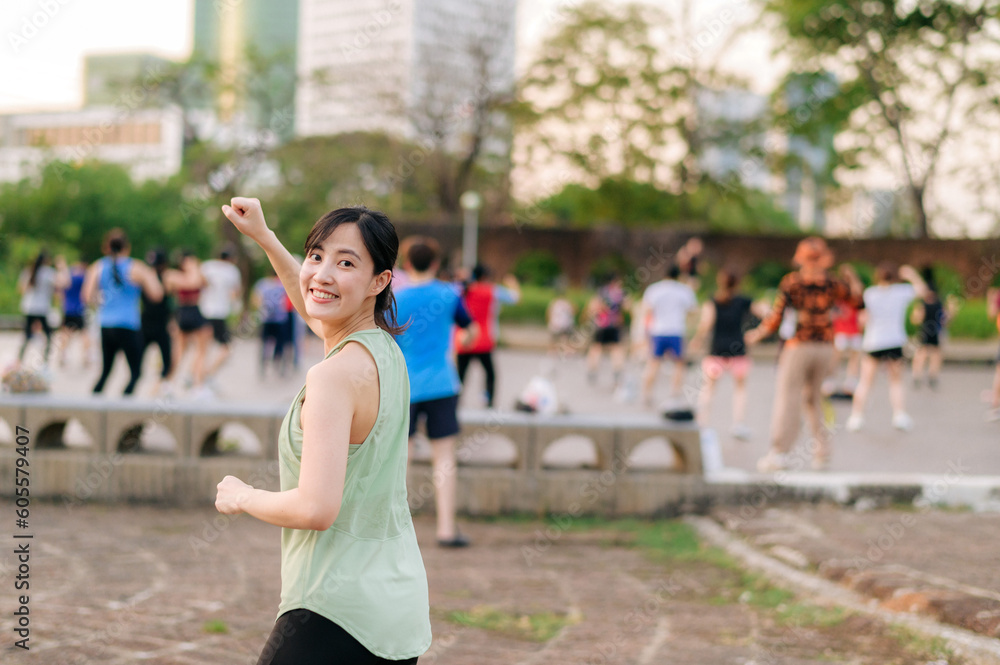 Obraz premium Female jogger. Fit young Asian woman with green sportswear aerobics dance exercise in park and enjoying a healthy outdoor. Fitness runner girl in public park. Wellness being concept