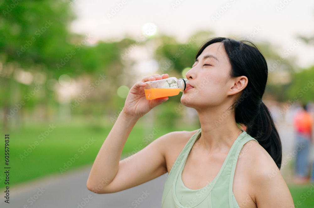 Female jogger. Fit young Asian woman with green sportswear drinking organic orange juice after running and enjoying a healthy outdoor. Fitness runner girl in public park. Wellness being concept Female jogger. Fit young Asian woman with green sportswear drinking organic orange juice after running and enjoying a healthy outdoor. Fitness runner girl in public park. Wellness being concept