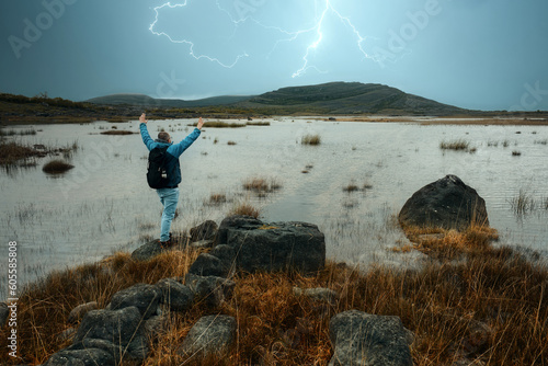 Man in blue jacket standing on the rock and watching thunderstorm over lake and mountains at Burren National Park in County Clare, Ireland 