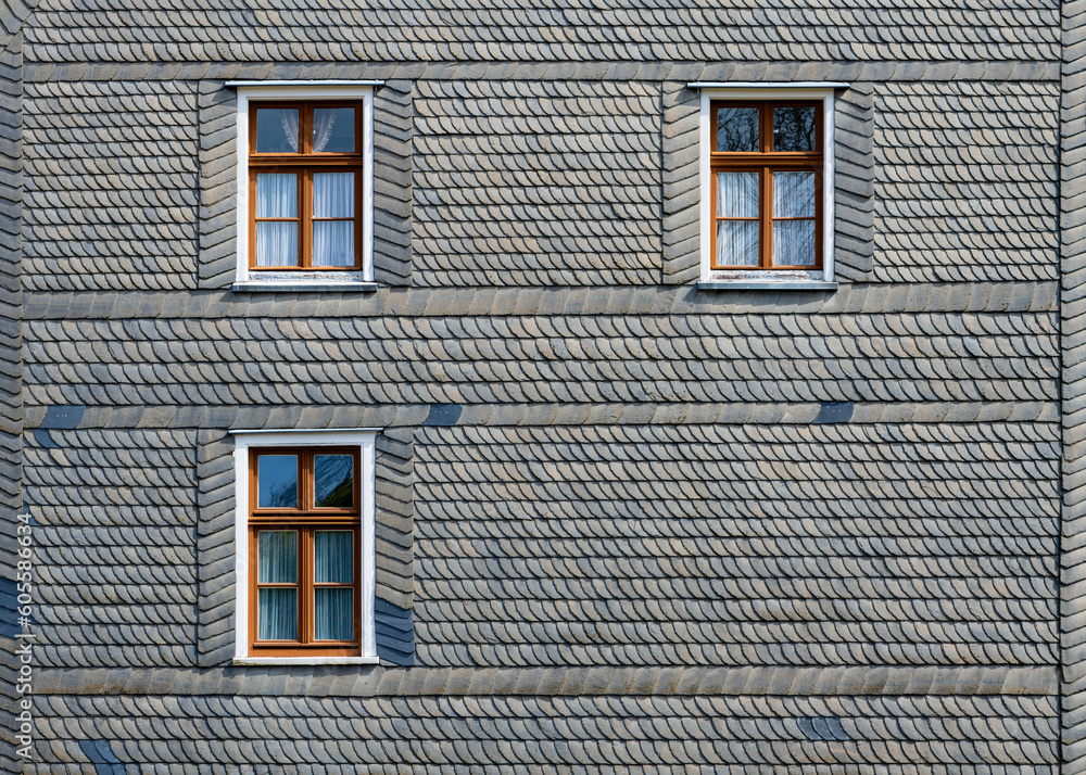 Slate facade of a historic building in Iserlohn Sauerland Germany with thee wooden window frames. Typical pattern made traditional craftmanship. Habitation in old town with half timbered houses. Slate facade of a historic building in Iserlohn Sauerland Germany with thee wooden window frames. Typical pattern made traditional craftmanship. Habitation in old town with half timbered houses.