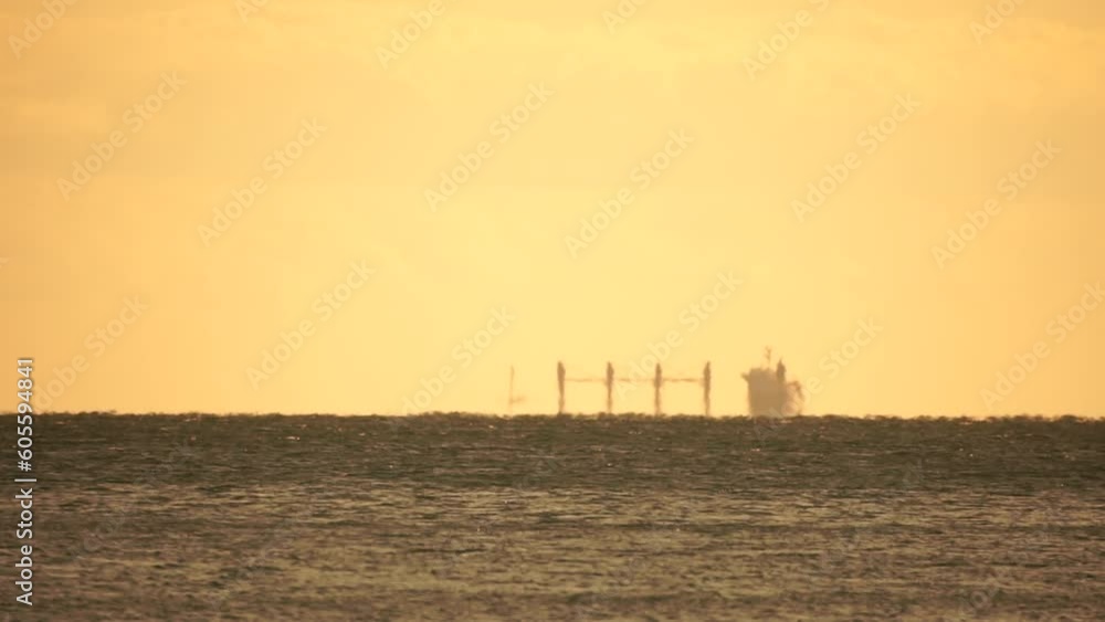 Mirage of cargo ship in the sea beyond the horizon. Ship sailing in the sea. Small waves on the golden surface of warm water with bokeh lights from the sun. Sea, nature and outdoor travel. Mirage of cargo ship in the sea beyond the horizon. Ship sailing in the sea. Small waves on the golden surface of warm water with bokeh lights from the sun. Sea, nature and outdoor travel.