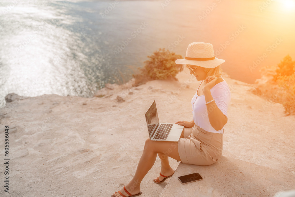 Naklejka premium Freelance women sea working on the computer. Good looking middle aged woman typing on a laptop keyboard outdoors with a beautiful sea view. The concept of remote work.
