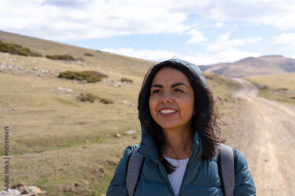 Beautiful latina woman smiling on a hiking day with a path and mountains in the background on a beautiful spring morning.l