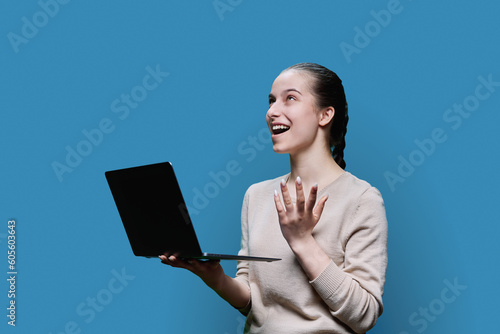 Surprised teen girl using laptop on blue studio background