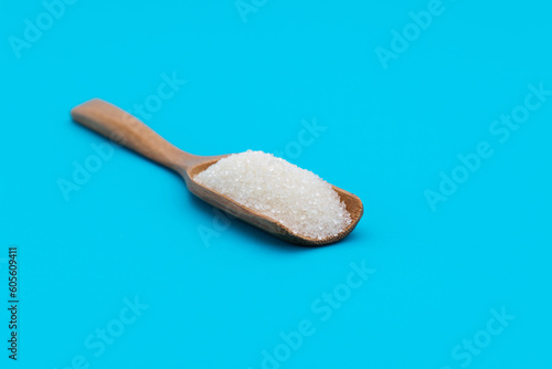 Wooden scoop with sugar crystals on blue background