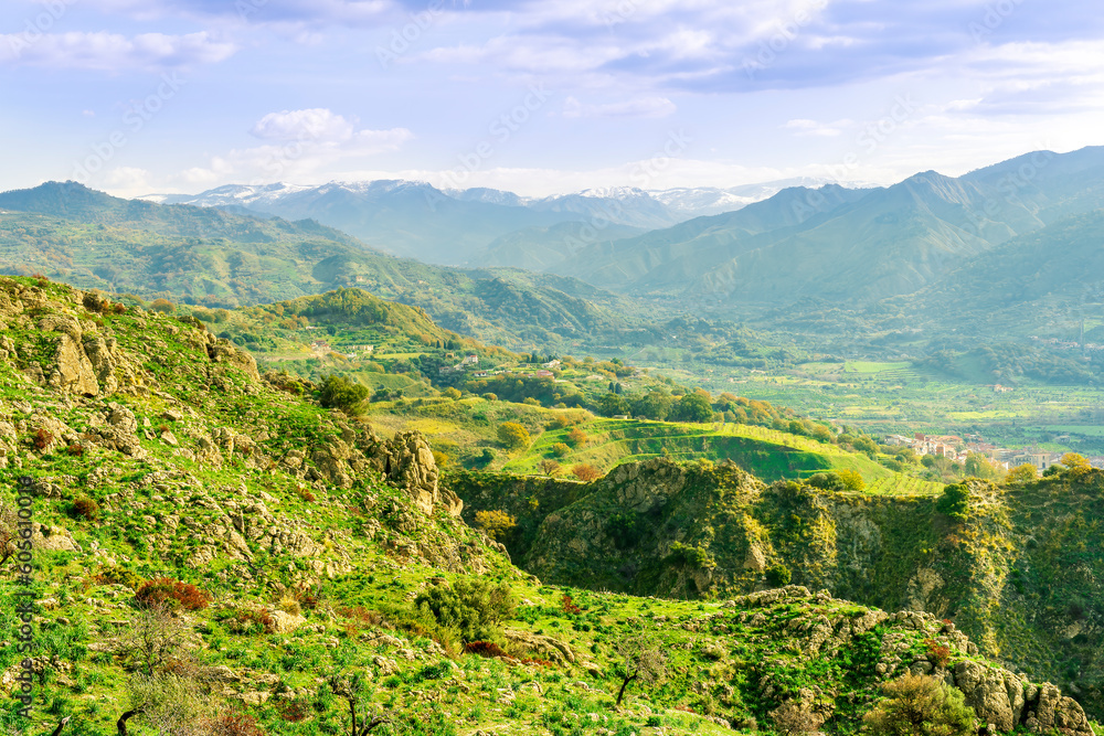 Naklejka premium picturesque view in a green mountain valley among slopes and hills with sunny plantations on a rocky plato and nice cloudy sunset on background
