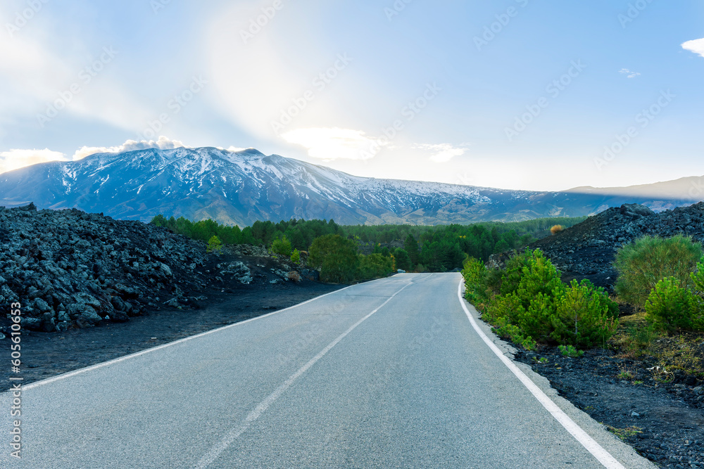 picturesque view of highland landscape of highway to mountain with old asphalt, blach sides with green forest and high snow mountain with amazin blue cloudy sky