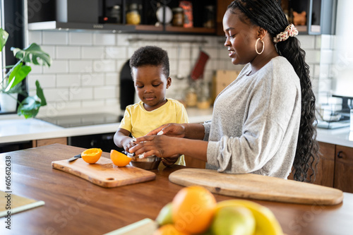 Cheerful African-American mother and son in the kitchen preparing a healthy fruit  snack and orange juice