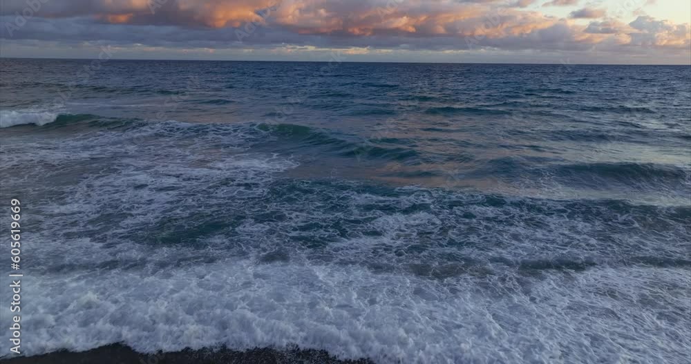 Sea waves break on shoreline at sunset with cloudy sky and horizon in background. Tilt-up view Sea waves break on shoreline at sunset with cloudy sky and horizon in background. Tilt-up view