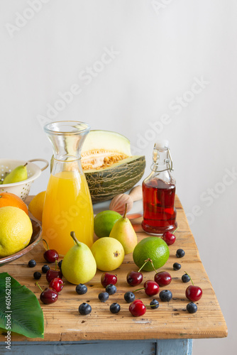 Top view of rustic table with summer fruits, bottle with orange and blueberry juice, white background, vertical, with copy space