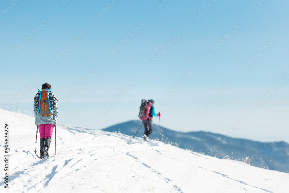two girls with backpacks walk along a path in the winter mountains. hiking in the mountains. two girls with backpacks walk along a path in the winter mountains. hiking in the mountains.