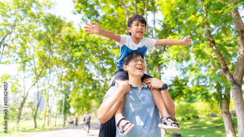 Happy Asian family enjoy and fun outdoor lifestyle travel together on summer holiday vacation. Father carrying and playing with little son at public park in the city. Family relationship concept.