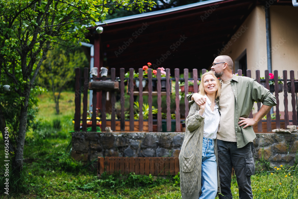 Caucasian happy relaxed middle age couple enjoying summer in country house standing on hugging in garden