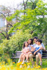 Happy Asian family parent and little kids enjoy and fun outdoor lifestyle on summer holiday vacation. Father, mother and child playing and resting together at park. Family relationship concept.