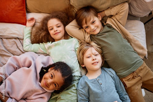 Top view at diverse group of children lying on bed together and looking at camera
