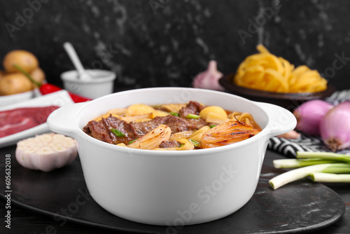 Pot of delicious vegetable soup with meat, noodles and ingredients on black wooden table