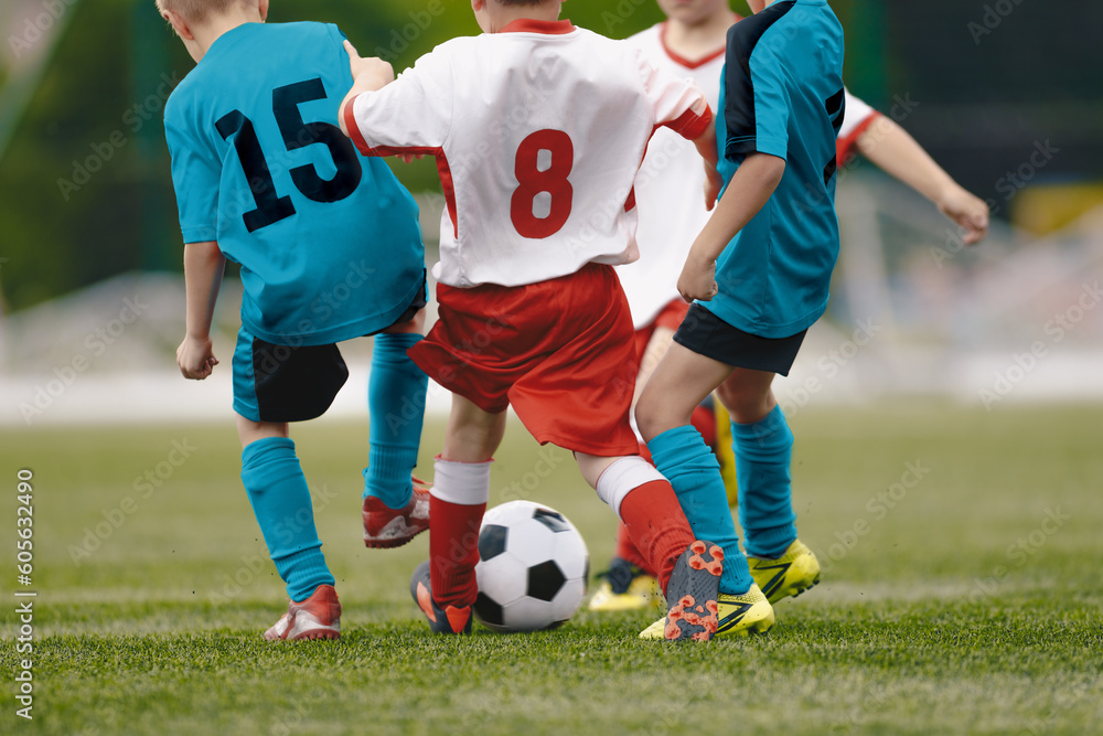 Anonymous group of elementary age children are playing soccer. Kids running and kicking a soccer ball. Boys wearing blue and red sports jerseys Anonymous group of elementary age children are playing soccer. Kids running and kicking a soccer ball. Boys wearing blue and red sports jerseys