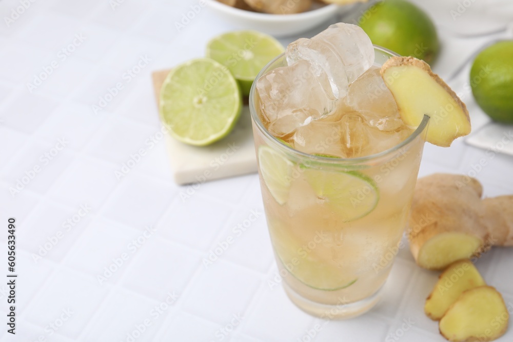 Glass of tasty ginger ale with ice cubes and ingredients on white tiled table, closeup. Space for text Glass of tasty ginger ale with ice cubes and ingredients on white tiled table, closeup. Space for text