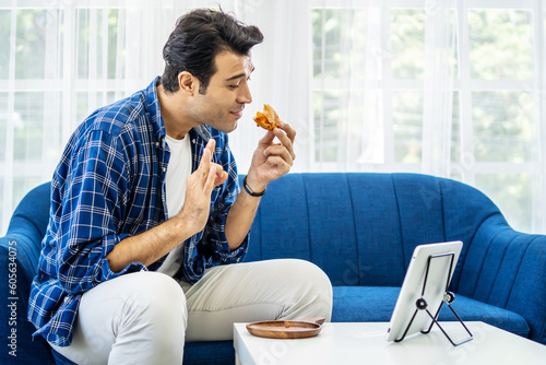 Caucasian man at home eating a slice of pizza food online together with her girlfriend in video conference with digital tablet for a online meeting in video call for social distancing