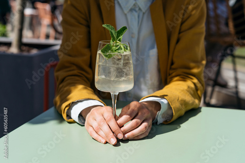 Drinking summer refreshing cocktail with ice. Female drinking hugo spritz in the city