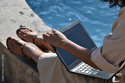 Woman sitting on a ledge and using a laptop at the sunlight