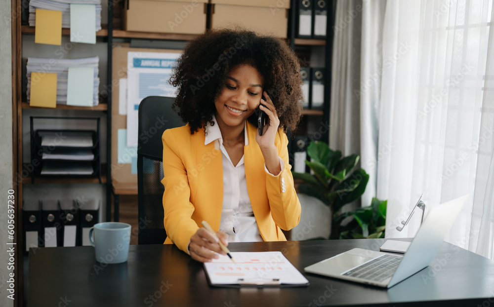Obraz premium Business African woman Talking on the phone and using a laptop with a smile while sitting at office