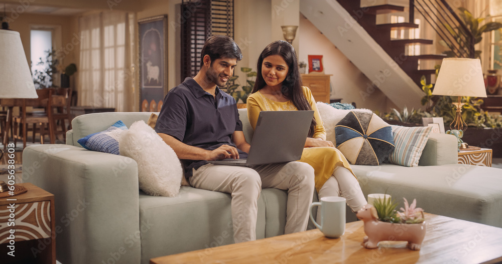 Portrait of Loving Young Indian Couple Enjoys Browsing Online Shopping Websites Together On A Laptop, While Sitting Cozily On Their Living Room Sofa. Browsing Interner, Choosing Products to Purchase Portrait of Loving Young Indian Couple Enjoys Browsing Online Shopping Websites Together On A Laptop, While Sitting Cozily On Their Living Room Sofa. Browsing Interner, Choosing Products to Purchase