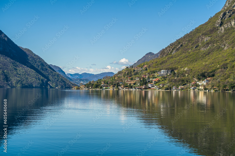 Lake Lugano surrounded by mountains and a small marina with moored boats on a sunny day