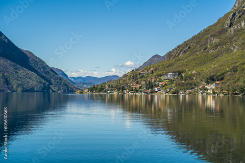 Lake Lugano surrounded by mountains and a small marina with moored boats on a sunny day