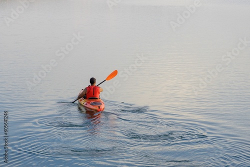Man on a kayak paddling in a calm lake under soft lighting at sunset