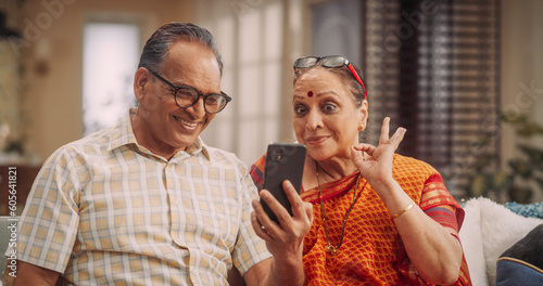 Elderly Couple Using Smartphone for Video Call at Home: Connecting with Family, Sharing Stories, and Celebrating Special Occasions. Cherishing Precious Moments Together. Medium Shot.