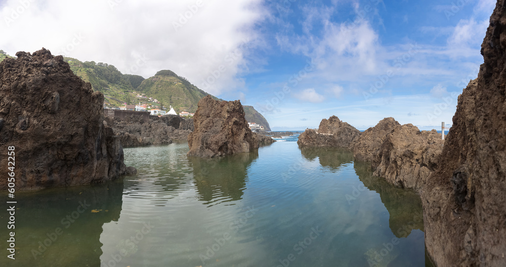 Panoramic view of the natural pools on village of Porto Moniz, formed by volcanic rocks, village buildings in the background, coast of the Madeira island, Portugal