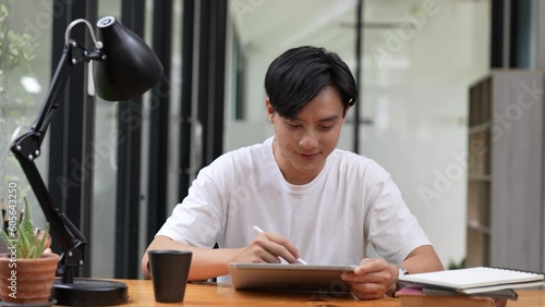 Positive asian guy using tablet for online communication, scrolling news feed, messaging in social media, Man holds tablet and smiling enjoy new mobile application on couch in living room at home
