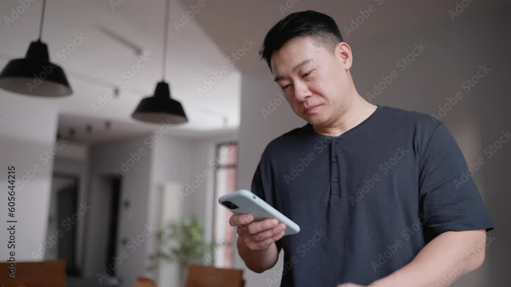 Pensive asian man texting on cellphone in kitchen at home Pensive asian man texting on cellphone in kitchen at home