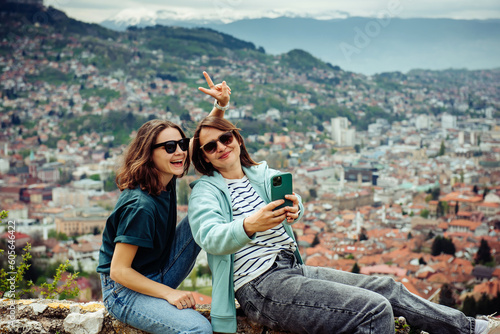 LGBT lesbian couple love moments together during travel vacation. Authentic people using smartphone against the background of a beautiful European city with orange roofs in the mountains