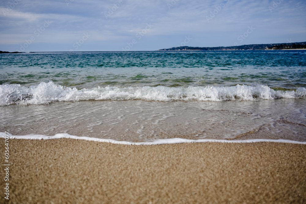 Scenic view of ocean waves splashing into the sandy beach with hills in the background Scenic view of ocean waves splashing into the sandy beach with hills in the background